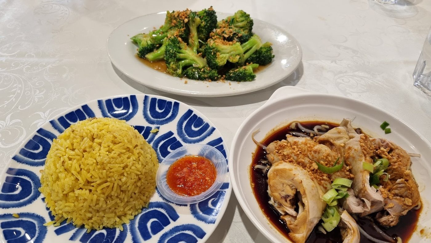 Hainanese chicken on rice with a small plate of greens and dipping sauce