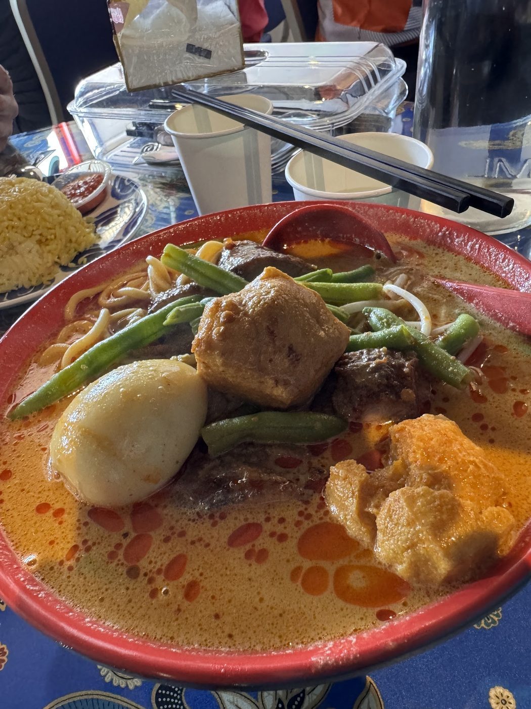 A bowl of curry noodles with tofu puffs, greens and sliced toppings